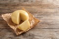 Parchment paper with cut wheel of delicious cheese on wooden table Royalty Free Stock Photo