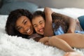 Parent child love. Happy young black woman embracing her little daughter on bed, cute girl laughing and enjoying hug