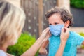 Parent with kid in face mask outdoor. Mother helping angry child to wear facemask during coronavirus and flu outbreak Royalty Free Stock Photo