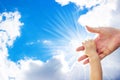 A one year old baby girl is grabbing her parent's hand, with a background of blue sky and white clouds