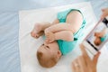 Parent taking photo of a baby with smartphone. Adorable newborn child taking foot in mouth Royalty Free Stock Photo