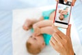 Parent taking photo of a baby with smartphone. Adorable newborn child taking foot in mouth Royalty Free Stock Photo