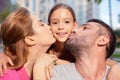 Joyful loving parents kissing their young daughter