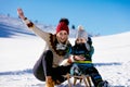 Parenthood, fashion, season and people concept - happy family with child on sled walking in winter outdoors