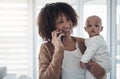 Parenting advice is just a call away. a young woman using a smartphone while carrying her adorable baby girl at home. Royalty Free Stock Photo