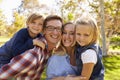 Parents carrying their two young kids in park look to camera