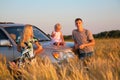 Parents and child sitting on car cowl on wheaten f