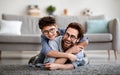 Parents and children being friends. Joyful father and son having fun, dad lying on floor, carrying boy on back Royalty Free Stock Photo