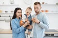 Parents and cute infant drinking delicious juice in kitchen