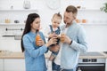 Parents and cute infant drinking delicious juice in kitchen