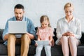 parents and cute little daughter sitting on couch and using digital