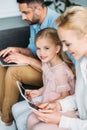parents with cute smiling daughter using digital devices