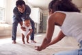 Parents Encouraging Smiling Baby Daughter To Take First Steps And Walk At Home Royalty Free Stock Photo