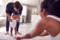 Parents Encouraging Smiling Baby Daughter To Take First Steps And Walk At Home Royalty Free Stock Photo