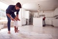 Parents Encouraging Smiling Baby Daughter To Take First Steps And Walk At Home