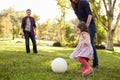 Parents kicking a ball with their young daughter in a park Royalty Free Stock Photo