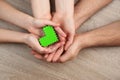 Parents and kid holding green heart in hands at wooden table, top view. Family day Royalty Free Stock Photo