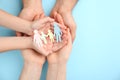 Parents and kid holding paper cutout of family in hands on turquoise background, top view. Space for text Royalty Free Stock Photo