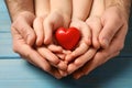 Parents and kid holding red heart in hands at light blue wooden table, closeup Royalty Free Stock Photo