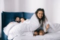 Parents lying in bed and looking at cute smiling daughter having fun under blanket Royalty Free Stock Photo