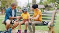 Parents, park bench and helmet with kid, help and safety for skating, rollerskate or bike. Interracial family, mom and