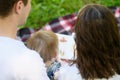 Parents reading a book to their child, sitting on a blanket during a picnic in the park, watching educational pictures Royalty Free Stock Photo