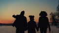 Parents silhouette holding hands going to river shore with daughter sunset view. Royalty Free Stock Photo