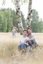 Parents sitting against tree while girl running at field Royalty Free Stock Photo