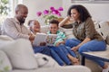 Parents Sitting On Sofa With Children At Home Reading Book Together Royalty Free Stock Photo