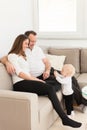 Parents sitting on the sofa and looking at their beautiful baby girl playing with cell phone. Royalty Free Stock Photo