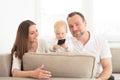 Parents sitting on the sofa. Their beautiful baby girl playing with cell phone. Royalty Free Stock Photo