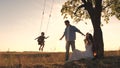 Parents swing a happy child high up on a swing at sunset, a cheerful family in the glare of the sun plays with their Royalty Free Stock Photo