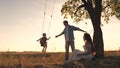 Parents swing a happy child high up on a swing at sunset, a cheerful family in the glare of the sun plays with their