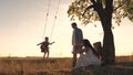 Parents swing a happy child high up on a swing at sunset, a cheerful family in the glare of the sun plays with their Royalty Free Stock Photo