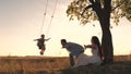 Parents swing the little girl on a swing on a summer day, flying like an airplane in the sky, happy mother and father