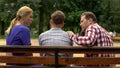 Parents talking with son on bench in park, supporting teen in time of trouble