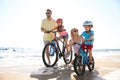 Parents teaching children to ride bicycles on sandy beach near sea Royalty Free Stock Photo