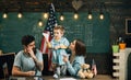 Parents teaching son american traditions playing. Kid with parents in classroom with usa flag, chalkboard on background Royalty Free Stock Photo