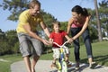 Parents Teaching Son To Ride Bike In Park Royalty Free Stock Photo