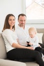 Parents and their beautiful baby girl sitting on the sofa and looking at the camera. Royalty Free Stock Photo