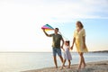 Happy parents with their child playing with kite on beach, space for text. Spending time in nature Royalty Free Stock Photo