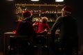 Parents and their little daughter in a Santa hat are sitting at a wooden table in a room with bright garlands. New Year. Christmas Royalty Free Stock Photo