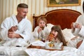 Best breakfast. Parents and two kids in white bathrobes having breakfast in bed, eating pastries and drinking coffee in Royalty Free Stock Photo