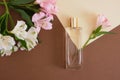 Parfum with flowers on beige brown background. A perfume bottle and white and pink lottle lily flowers