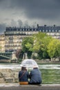 2 people take shelter under their umbrella in the middle of summer in Paris along Seine River