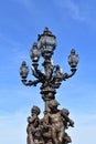 Pont Alexandre III detail, bronze streetlight with sculptures and blue sky. Paris, France.