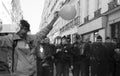 A protestor dressed up as a clown with a balloon stands next to French riot police