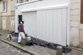 African American man worker paints walls of facade house with white paint. External outdoors repair