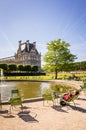 A man sunbathing on a metal lawn chair by a basin in the Tuileries garden in Paris with the Louvre palace in the background Royalty Free Stock Photo