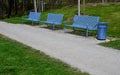 Park benches in light blue made of metal strips similar to a lattice. trash can and beautiful lawn with park paths of gravel thres